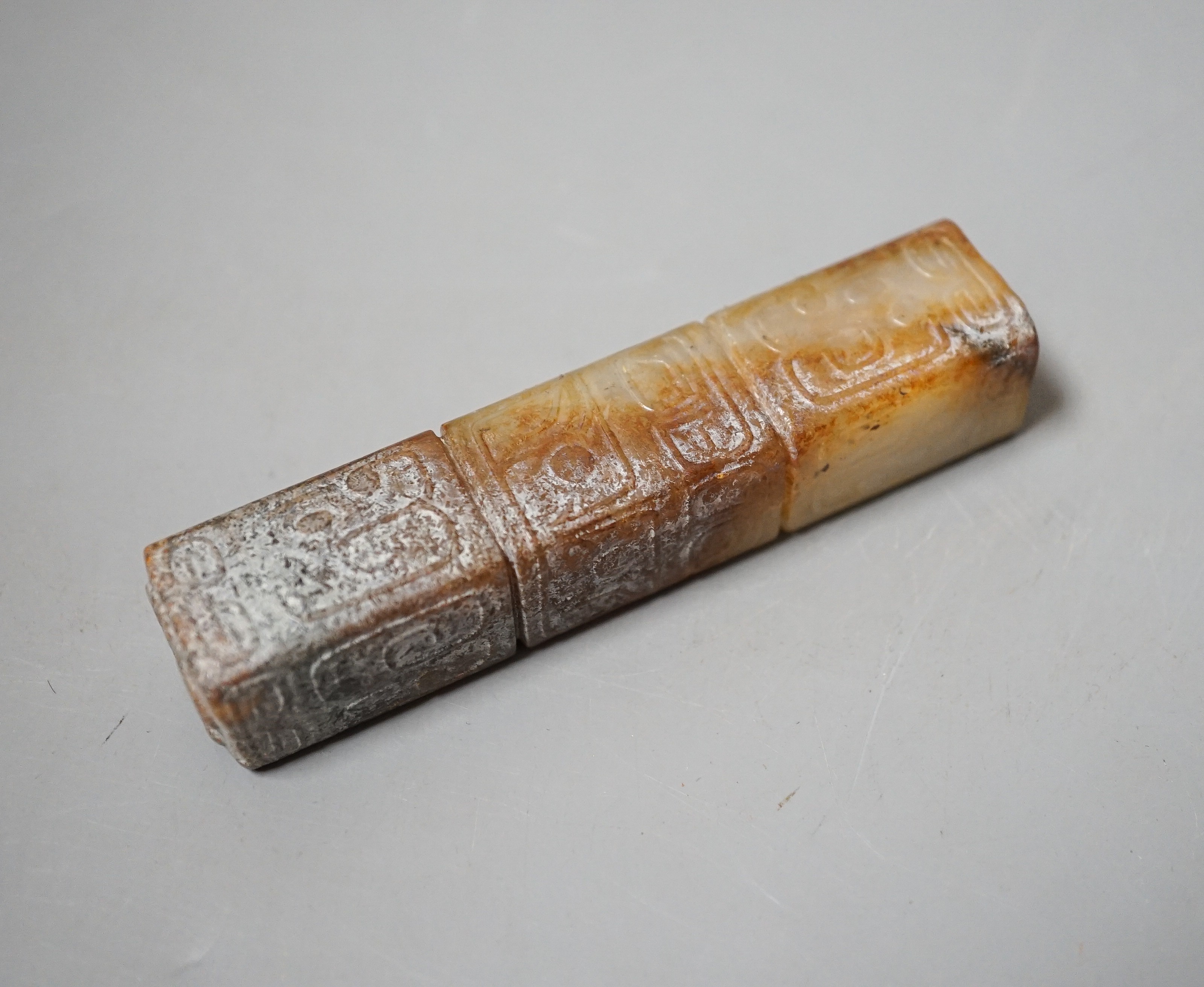 A Chinese archaistic white and russet jade handle mount, carved in relief with three registers of taotie masks, height 9.7cm